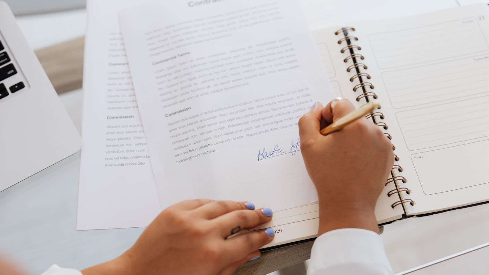 A person signing a contract that lists commission and commercial terms, representing human approval of AI-assisted work