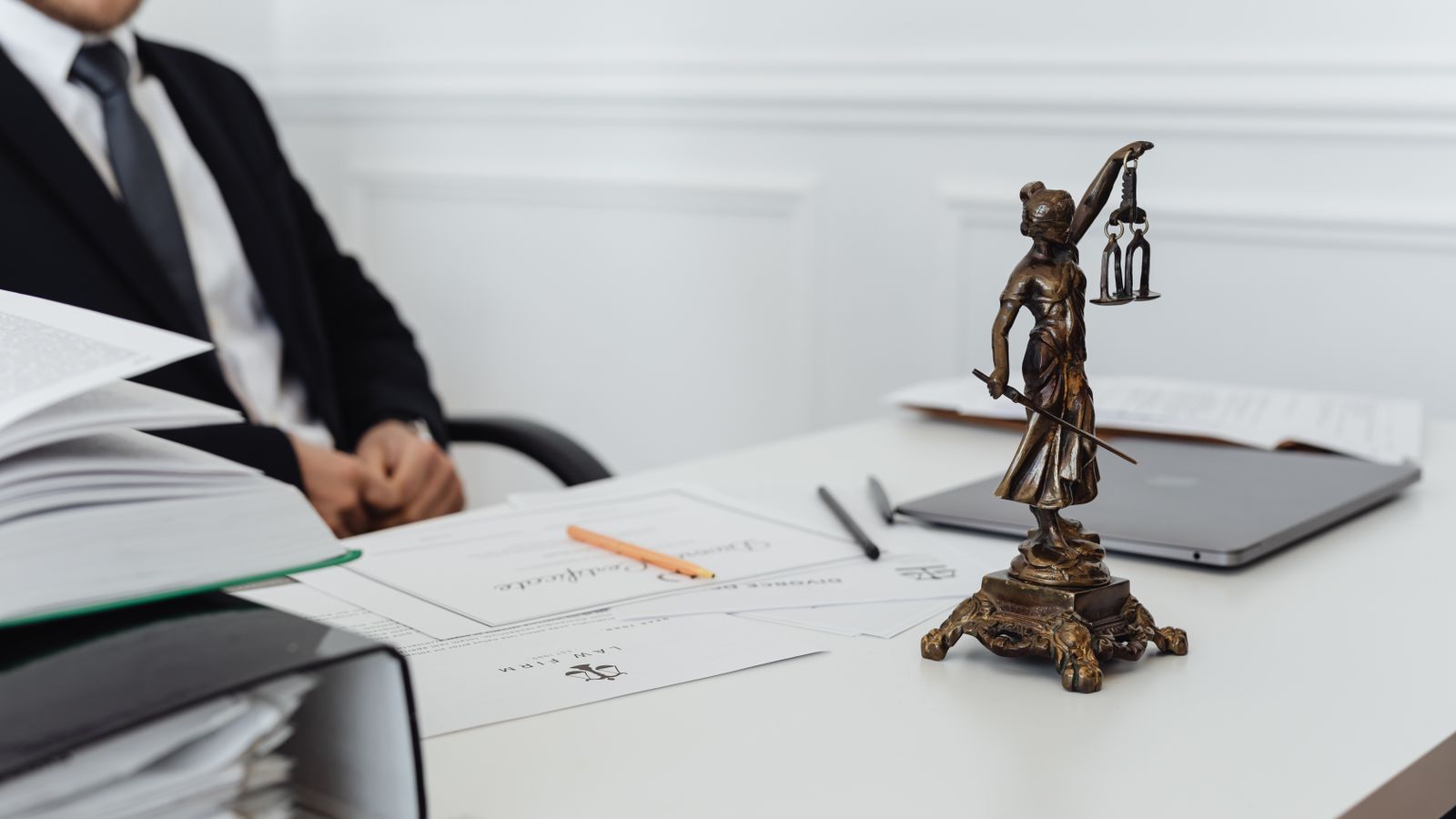A bronze Lady Justice statue on a desk beside legal documents and a laptop, representing insurance AI regulation